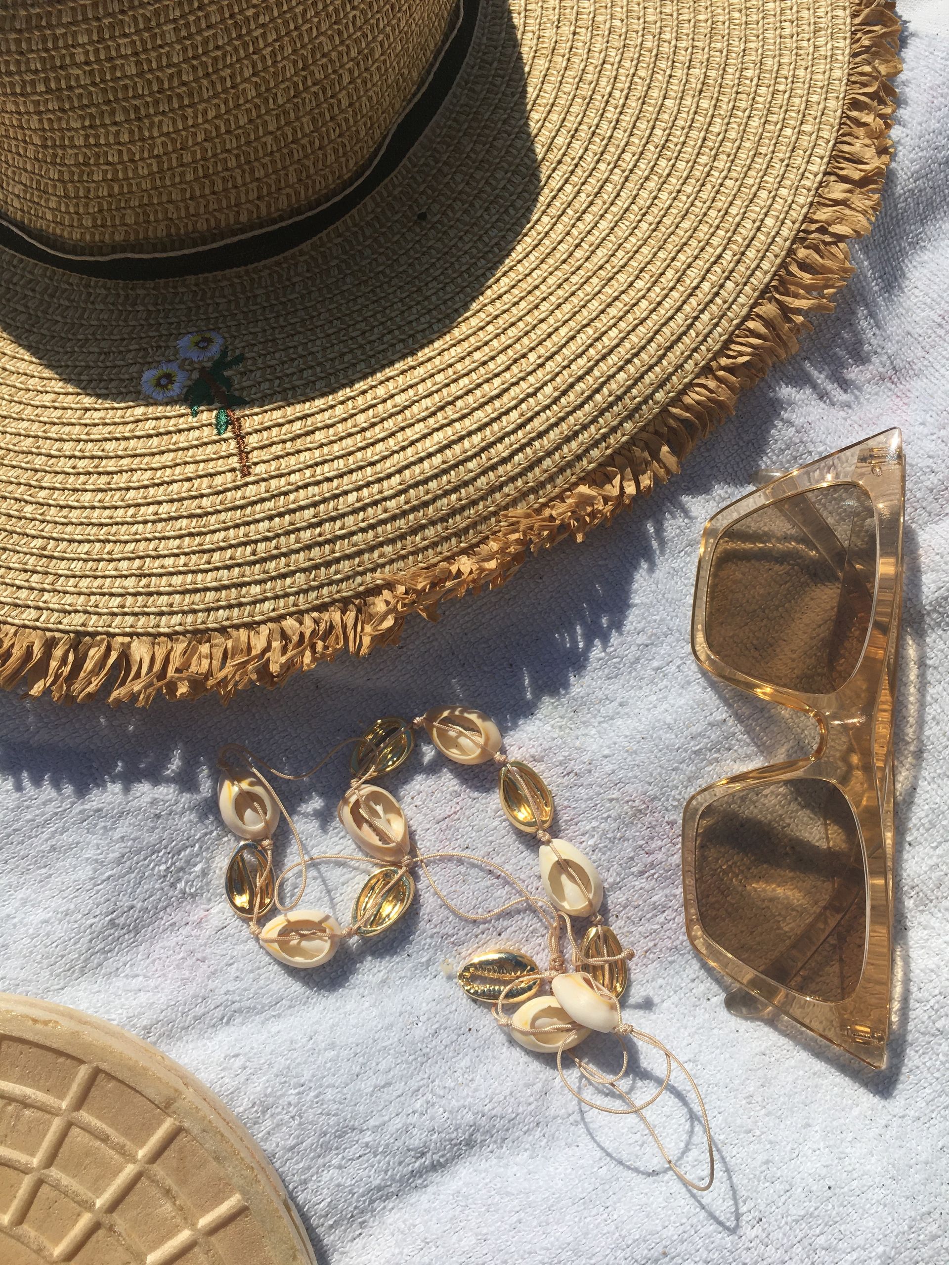 Close-up of a straw hat, sunglasses, and shell necklace on a towel, perfect for a beach day.