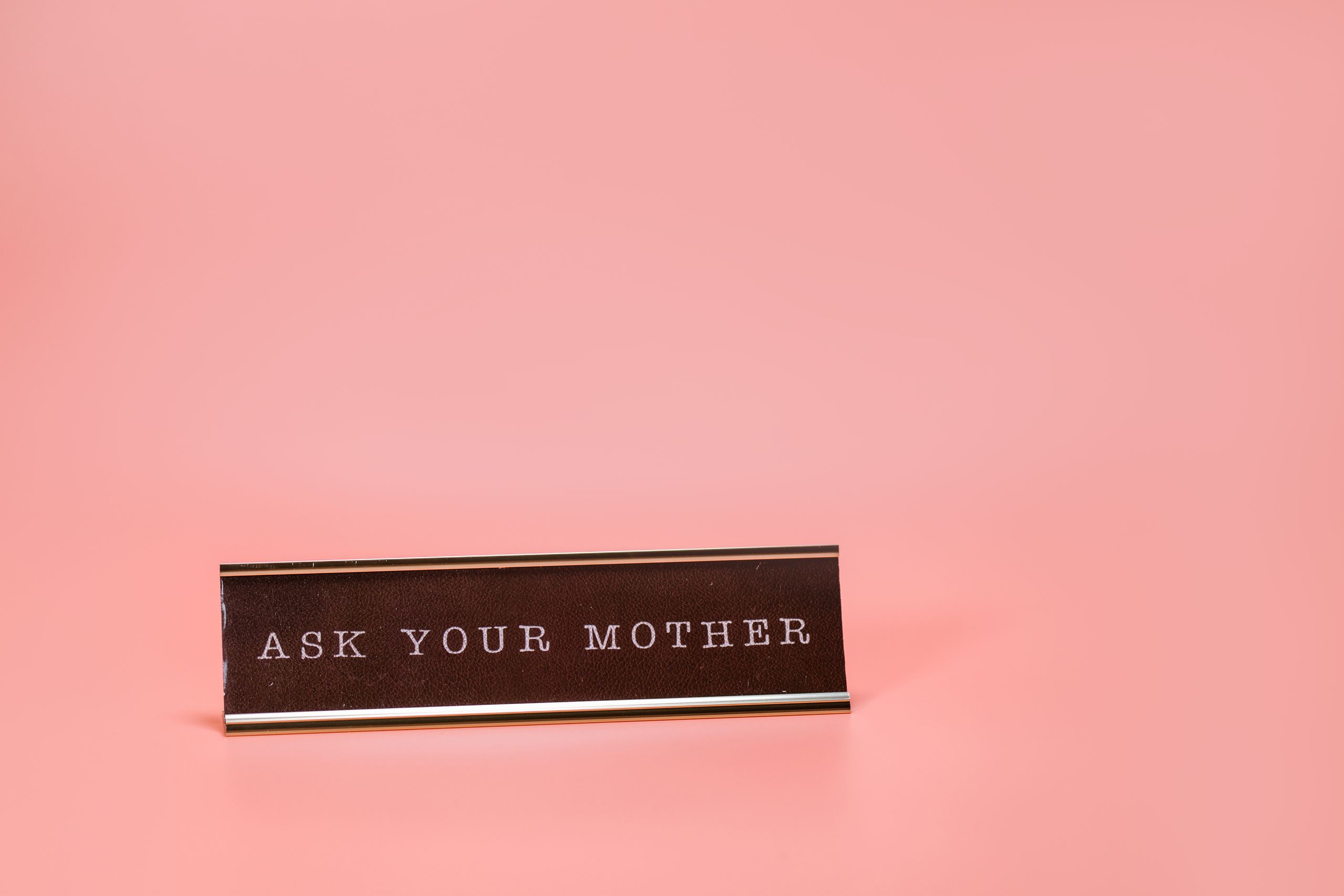 Humorous desk sign with 'Ask Your Mother' text on a pink backdrop.