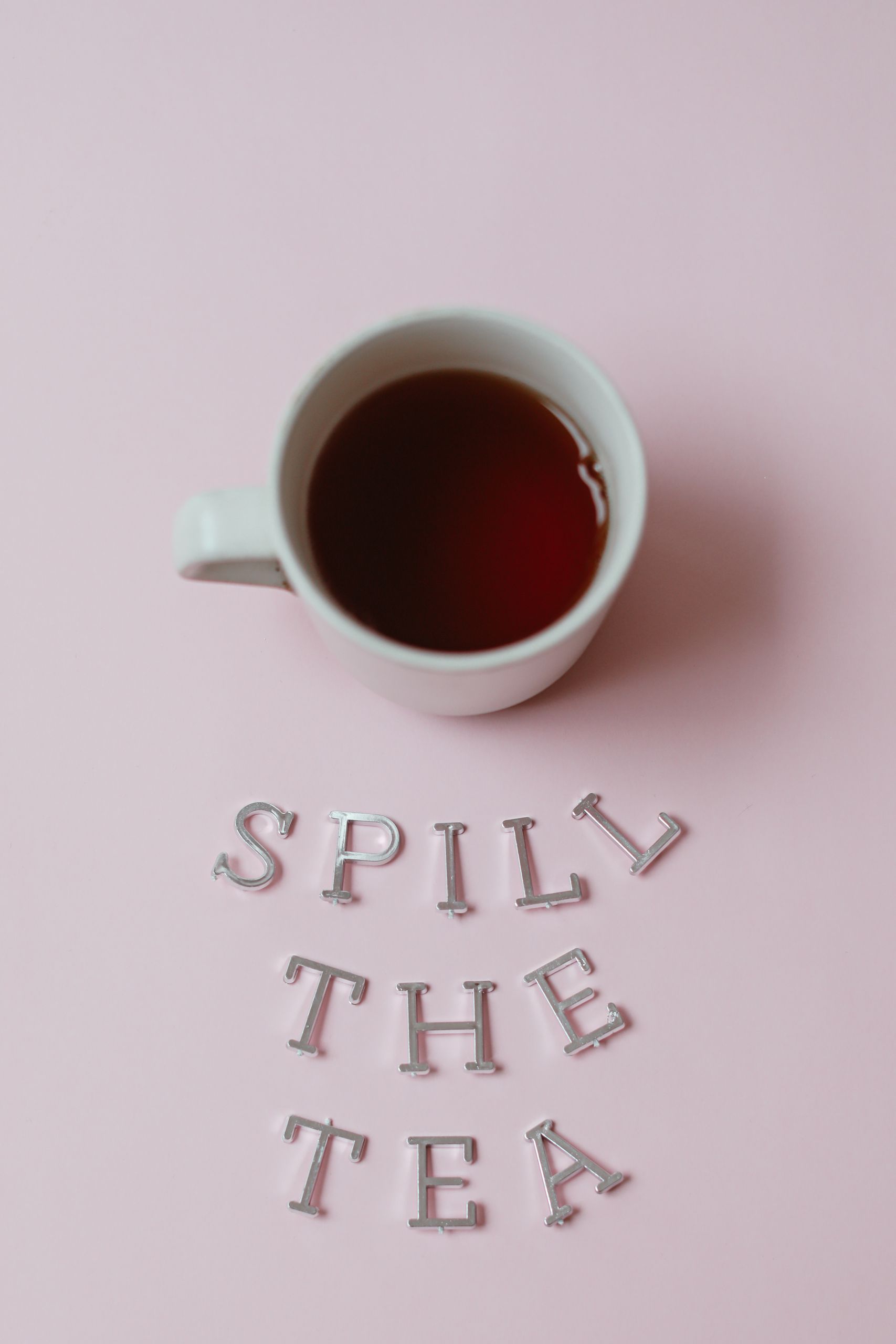 Minimalistic photo of a cup of tea with "Spill the Tea" text on a pink surface.